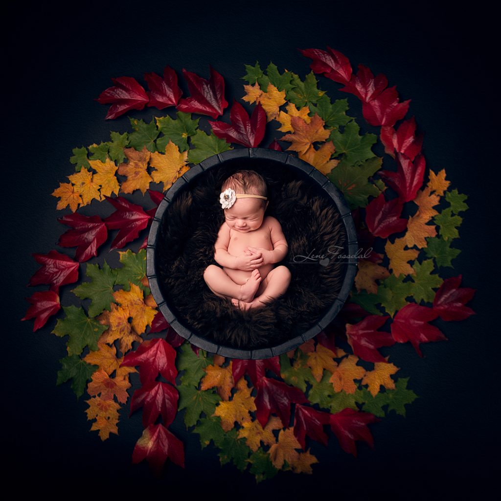 En modellbaby som ligger i en kurv, omringet av høstblader.