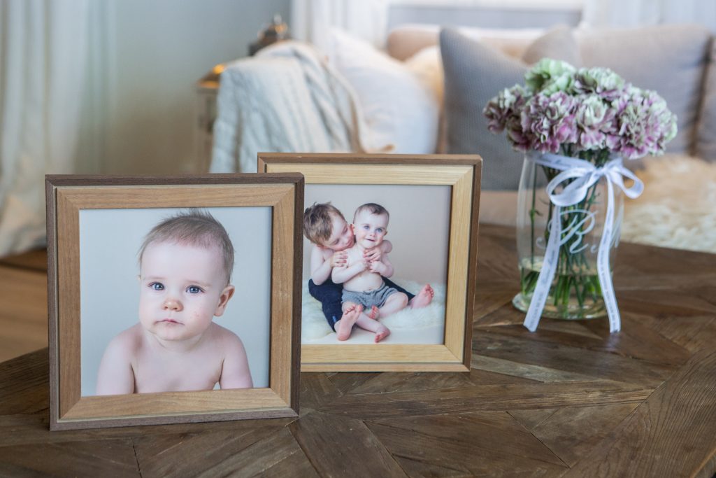 To bilder i rammer på et bord. Det er barn på bildene. På bordet står det også en vase med blomster. Dette viser hvorfor dere bør printe hos meg.