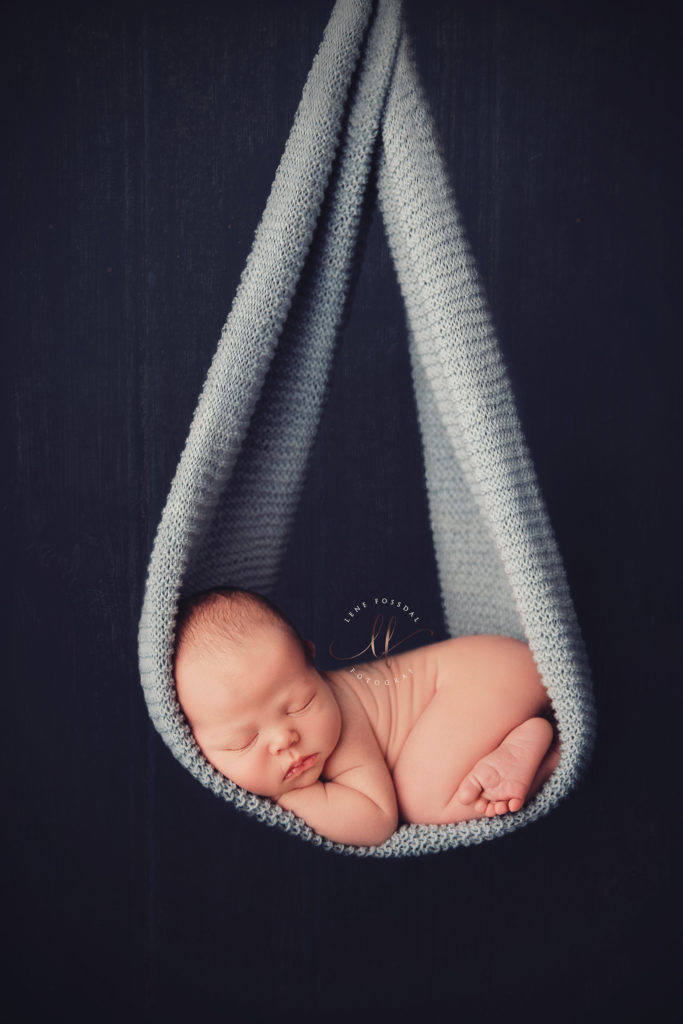 Et baby hengende i et pledd. Dette er ikke ekte, og baby ligger egentlig trygt på en beanbag.