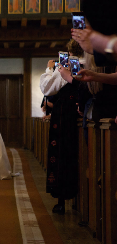 Bilde av gjester i en kirke som står med mobilene sine. Dette er typisk for mobilbruk i bryllup.