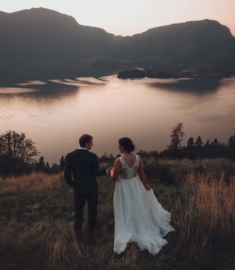 Brudepar foran en av de norske fjordene. Mannen holder bruden i hånden og leder vei, og de går bort fra kamera mot fjorden.